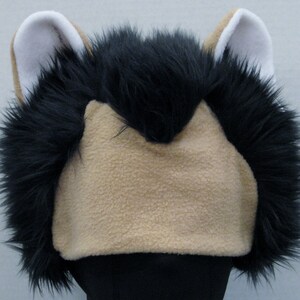 May include: A black and tan furry animal head costume with white ears. The costume is made of soft, plush fabric and has a realistic look.