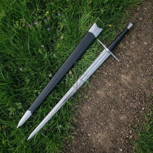 May include: A long steel sword with a straight crossguard and a black handle, positioned next to a matching black scabbard with silver-toned metal fittings at the tip and throat. The blade is double-edged and tapers to a sharp, pointed tip.