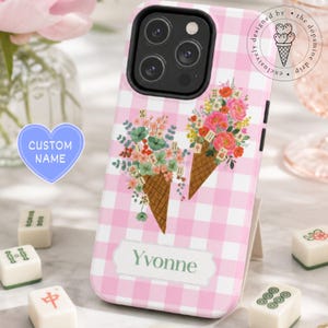 May include: A pink and white gingham phone case featuring two ice cream cones filled with colourful flowers and mahjong tiles. The case includes a rectangular label with the name Yvonne printed in green text on the lower portion of the cover.
