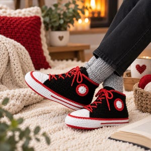 Puede incluir: Un par de zapatillas altas tejidas a mano a ganchillo con parte superior negra, puntera blanca y cordones rojos. Los zapatos tienen una suela blanca con una franja roja y un parche circular blanco y rojo en el lateral.