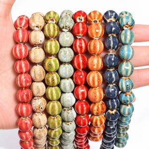 May include: Eight vertical strands of round ceramic beads in various colours including red, beige, green, light green, orange, dark blue, and light blue. Each bead features a ribbed texture with a glossy finish and a central hole for stringing.
