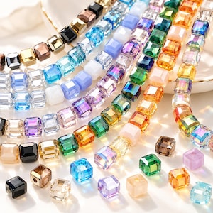 Può includere: Una collezione di perline quadrate in vetro multicolore disposte in fili paralleli e sparse singolarmente. Le perline presentano un mix di finiture traslucide, opache e iridescenti nelle tonalità del blu, verde, arancione, viola, nero e trasparente.