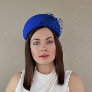 May include: A royal blue felt hat with a black netting detail. The hat is shaped like a half-circle and sits on the head.