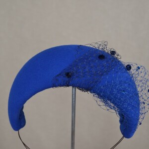 May include: A blue felt hat with a black net veil and blue sequins. The hat is shaped like a crescent moon and has a headband.