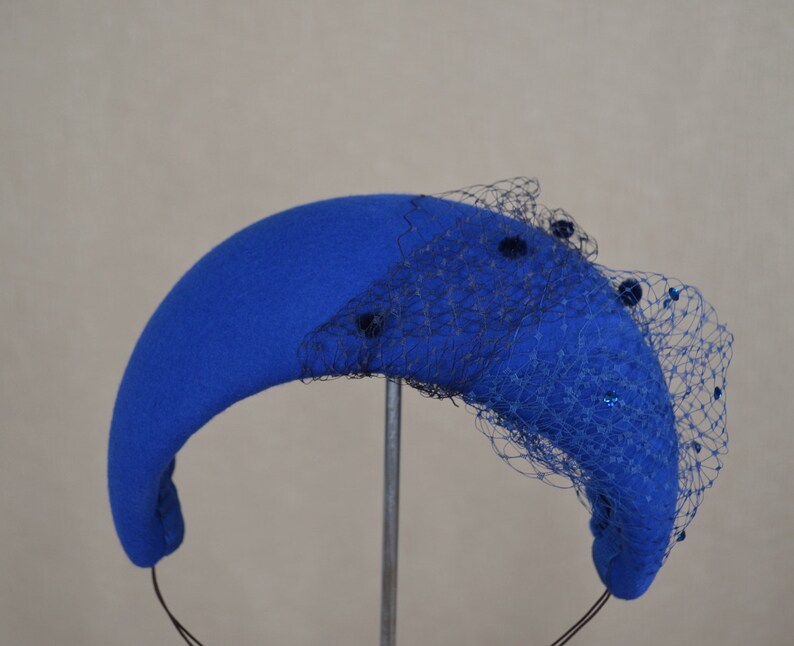May include: A blue felt hat with a black net veil and blue sequins. The hat is shaped like a crescent moon and has a headband.