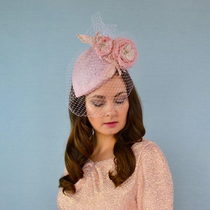 May include: A pink felt hat with a veil and two pink fabric flowers. The hat is tilted slightly to the side.