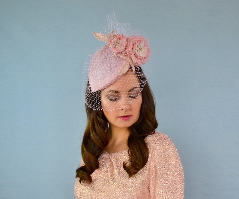 May include: A pink felt hat with a veil and two pink fabric flowers. The hat is tilted slightly to the side.