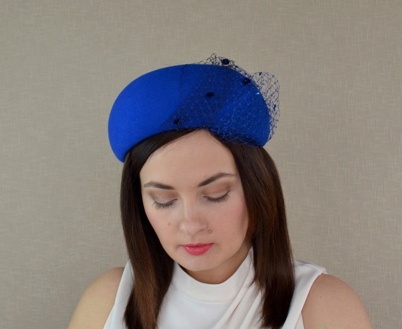 May include: A royal blue felt hat with a black netting and small black beads. The hat is tilted slightly to the side.
