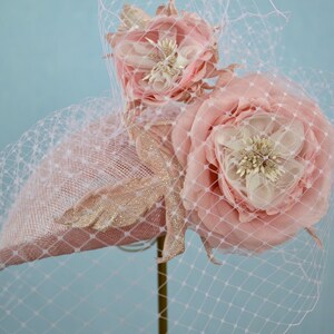 May include: A pink hat with a veil and two large pink fabric flowers. The hat is decorated with gold glitter.