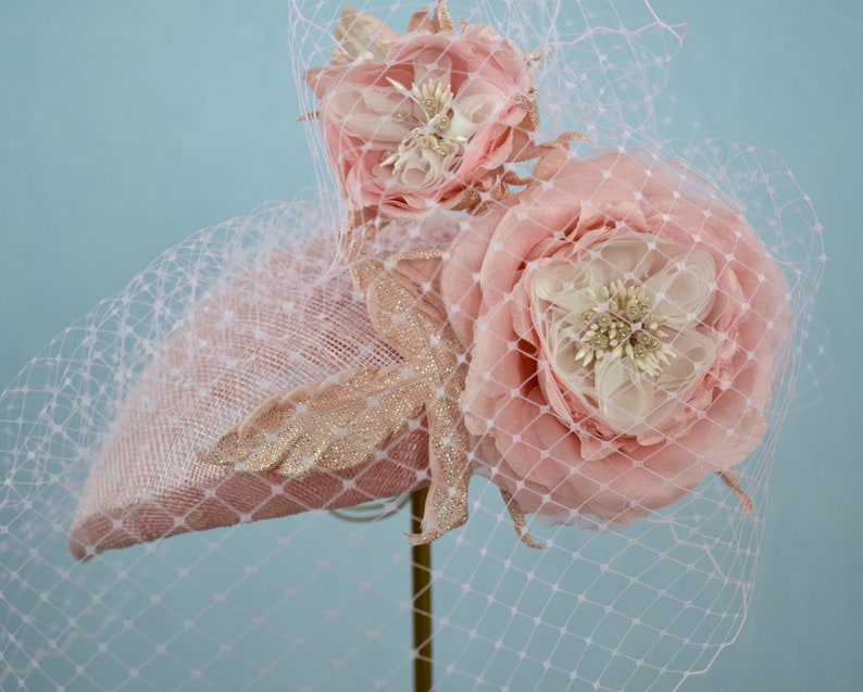 May include: A pink hat with a veil and two large pink fabric flowers. The hat is decorated with gold glitter.