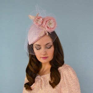 May include: A pink hat with a veil and two pink fabric flowers. The hat is tilted slightly to the side.