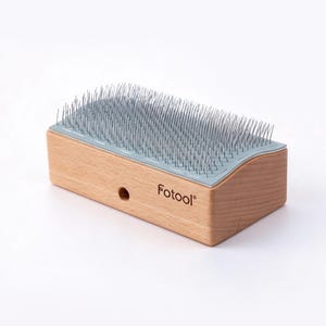 Puede incluir: Un cepillo cardador rectangular para mascotas con mango de madera clara y una base azul claro con numerosas púas metálicas finas. El nombre de la marca Fotool está impreso en color marrón oscuro en el lateral del bloque de madera.