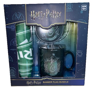 May include: A Harry Potter banner flag bundle in a dark blue box featuring a green and white striped banner, a round Slytherin coaster, and a black mug with a Slytherin crest. The packaging includes the text Harry Potter, Banner Flag Bundle, 1 Mug, 1 Felt League Flag & 1 Coaster, and Age 13+.