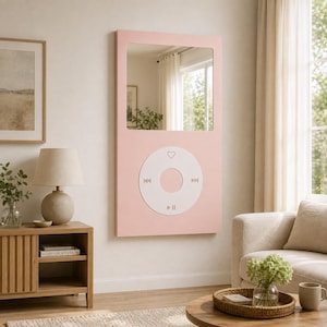 May include: A rectangular wall mirror featuring a light pink frame designed to resemble a vintage digital music player. The mirror includes a large white circular control interface at the bottom with icons for play, pause, skip, and a heart symbol.