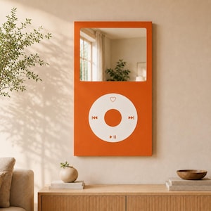 May include: A rectangular orange wall mirror designed to resemble a classic digital music player. The top section features a reflective glass surface, while the bottom portion displays a white circular control interface with a heart, skip, and play icons.