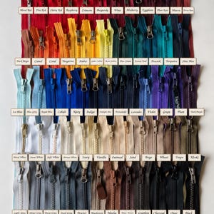 Puede incluir: Una colección de numerosas cremalleras dispuestas en filas por color, con un amplio espectro de tonos que incluyen rojos, naranjas, amarillos, verdes, azules, morados, blancos, beiges y grises, cada una etiquetada con su nombre de color.