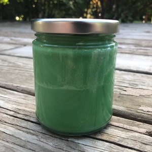 May include: A glass jar with a silver lid filled with a green substance.