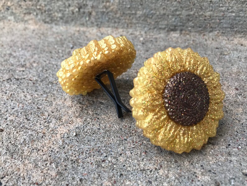 May include: Two gold glitter sunflower car air fresheners. The sunflowers have a brown glitter center.