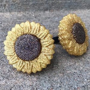 May include: Two gold glitter sunflower hair scrunchies with brown glitter centers.
