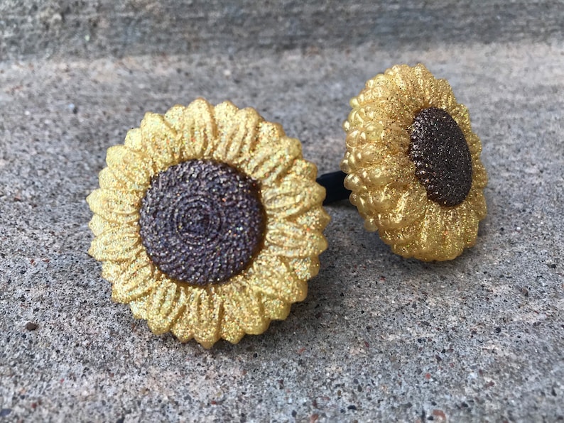 May include: Two gold glitter sunflower hair scrunchies with brown glitter centers.