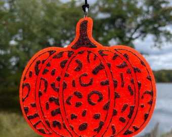 May include: Orange pumpkin-shaped ornament with a black leopard print design. The ornament is hanging from a black string.