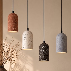 Pode incluir: Quatro candeeiros suspensos cilíndricos com acabamento em mosaico salpicado nas cores terracota, creme, preto e cinzento. Cada luminária pende de um fio preto fino e apresenta um topo arredondado, iluminando para baixo a partir da base.