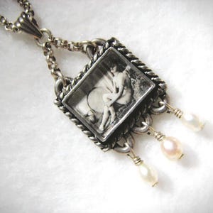 May include: Silver-toned pendant necklace featuring a rectangular pendant with a black and white image of a classical figure. The pendant is framed with a twisted rope design and hangs from a chain. Three small, dangling pearls add a delicate touch.