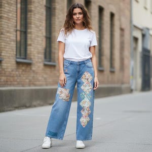 Op de afbeelding: Een effen wit T-shirt met korte mouwen gecombineerd met een lichtblauwe wijde spijkerbroek. De broek heeft een reeks ruitvormige bloemenstoffen patches op het linkerbeen en een rechthoekige patch op de rechterdij. Witte sneakers maken de outfit af.