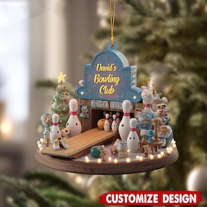 May include: A hanging ornament featuring a bowling alley scene with a blue sign reading David's Bowling Club. The display includes white bowling pins, a wooden lane, a small Christmas tree, and miniature bowling balls on a circular wooden base.