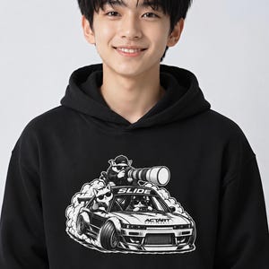 May include: A black hooded sweatshirt featuring a graphic print of a car drifting with smoke. The car contains cats wearing sunglasses, with one cat on the roof holding a large camera lens. The text SLIDE and ACTART are printed on the car.