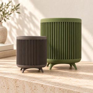 May include: Two cylindrical planters with vertical slats and small feet. The smaller planter is dark gray, and the larger planter is olive green. Both containers feature a uniform, ribbed exterior design and an open top, providing a structured look.