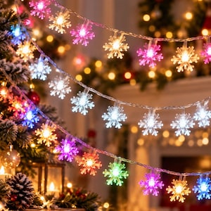 Puede incluir: Una cadena de luces LED con cubiertas translúcidas en forma de copo de nieve. Los copos emiten luz multicolor, incluyendo tonos rosa, blanco, amarillo y verde, dispuestos a lo largo de un cable fino, flexible y transparente.