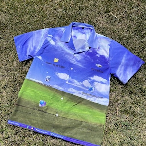 May include: A short-sleeved button-down shirt featuring a digital desktop wallpaper print with a blue sky, white clouds, and green grass. Icons labeled super secret folder, my hardrive, new document, gmogmogma.com, and th is computer are printed on the front.