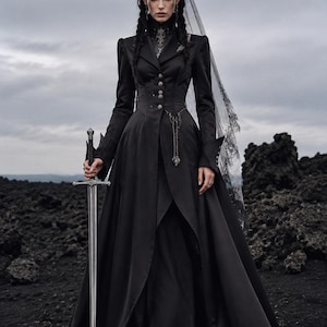 May include: A long-sleeved black coat dress with a high collar, silver buttons, and a flared skirt. The garment features a silver chain accessory at the waist and is paired with a black lace veil headpiece. A silver sword is held in one hand.