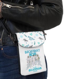 Può includere: Borsa a tracolla bianca e turchese con la scritta "Backstreet Boys" e una foto di gruppo. La patta della borsa presenta un motivo di cuori, fiocchi di neve e aerei turchesi. È visibile anche il testo "into the MILLENNIUM Las Vegas".