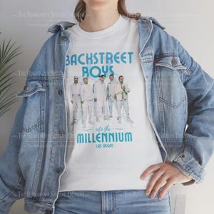 May include: White t-shirt with the Backstreet Boys band image and the text "BACKSTREET BOYS" in blue. The text "into the MILLENNIUM LAS VEGAS" is below the image. The shirt is worn with a light blue denim jacket.