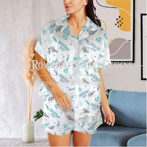 May include: White satin pyjama set featuring a pattern of teal hearts, snowflakes, and airplane graphics. The text "Backstreet Boys" is repeated throughout the design. The set includes a button-down shirt and shorts.