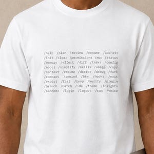 Puede incluir: Una camiseta blanca de manga corta con un bloque de texto negro impreso en el pecho. El texto consta de varios términos de estilo línea de comandos que comienzan con barras inclinadas, incluidos help, plan, review, rename, add-dir, init, clear.