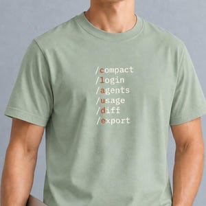 以下が含まれることがあります： セージグリーンの半袖Tシャツ。前面には「/compact」「/login」「/agents」「/usage」「/diff」「/export」というコマンドリストが白い文字でプリントされています。各コマンドの「c」の文字は、落ち着いたオレンジ色で強調されています。