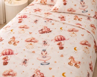 Puede incluir: Una sábana y dos fundas de almohada blancas con un patrón repetitivo de ilustraciones rosas que incluyen bailarinas, globos aerostáticos, caballos de juguete, trenes, zapatillas de ballet, nubes, estrellas y lunas sobre tela suave.