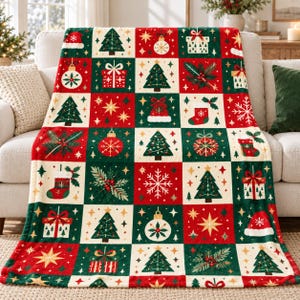 May include: A soft throw blanket featuring a repeating grid pattern of Christmas-themed icons including green pine trees, red and white gift boxes, ornaments, stockings, Santa hats, snowflakes, and holly sprigs on a red, green, and cream background.