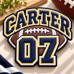 May include: A custom embroidered patch featuring a brown football with white laces in the centre. The name CARTER is arched in navy blue letters with yellow and white borders above the football, and the number 07 is in navy blue below.