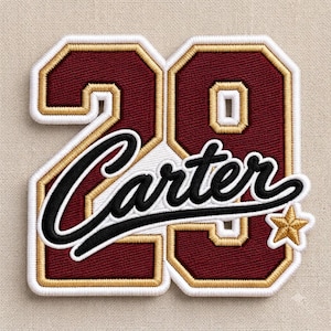 May include: A maroon and gold embroidered patch featuring the number 29 with the name Carter written in black script across the centre. The design includes a small gold star at the bottom right corner, all outlined in thick white stitching.