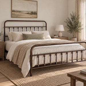 May include: A dark bronze metal bed frame featuring a rounded headboard and footboard with vertical spindle detailing. The bed is dressed in a white duvet, two matching pillows, and a long, textured olive green rectangular accent pillow.