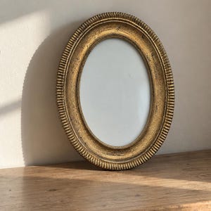 May include: An oval-shaped picture frame with a distressed gold finish and a textured, ribbed outer edge. The frame features a smooth, plain white center insert, providing a neutral space for a photograph or artwork within the decorative border.