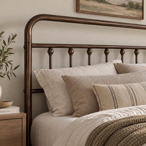 May include: A metal bed frame with a dark bronze finish featuring a rounded top rail and vertical spindles with spherical accents. The bed is dressed with light beige pillows, a textured tan lumbar pillow, and a striped accent pillow.