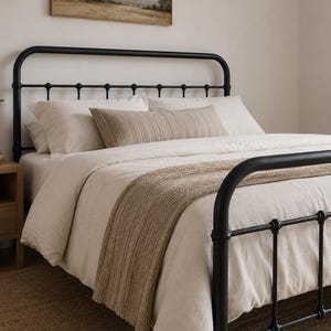 May include: A black metal bed frame with a rounded headboard and footboard featuring horizontal bars and spherical accents. The bed is dressed in cream-colored bedding, including two standard pillows, a long lumbar pillow, and a textured throw.