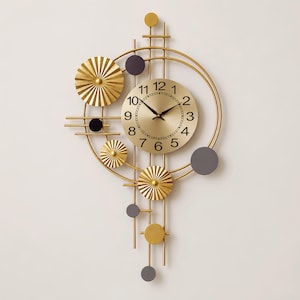Puede incluir: Un reloj de pared dorado con una esfera circular que presenta números y manecillas negras. El reloj está rodeado por un marco geométrico de varillas metálicas doradas, discos dorados plisados y acentos circulares gris oscuro asimétricos.