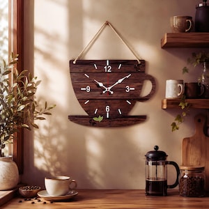 May include: A wall clock shaped like a coffee cup, crafted from dark brown horizontal wooden planks. It features white hour markers, white clock hands, and a jute rope hanger. Small decorative green leaves and coffee bean icons are visible.