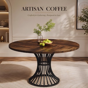 Peut inclure: Une table à manger ronde avec un plateau en bois brun foncé à motif chevrons et un pied central en métal noir composé de lattes verticales incurvées. Sur la table se trouvent un vase en verre avec des branches vertes et un bol en bois de pommes.
